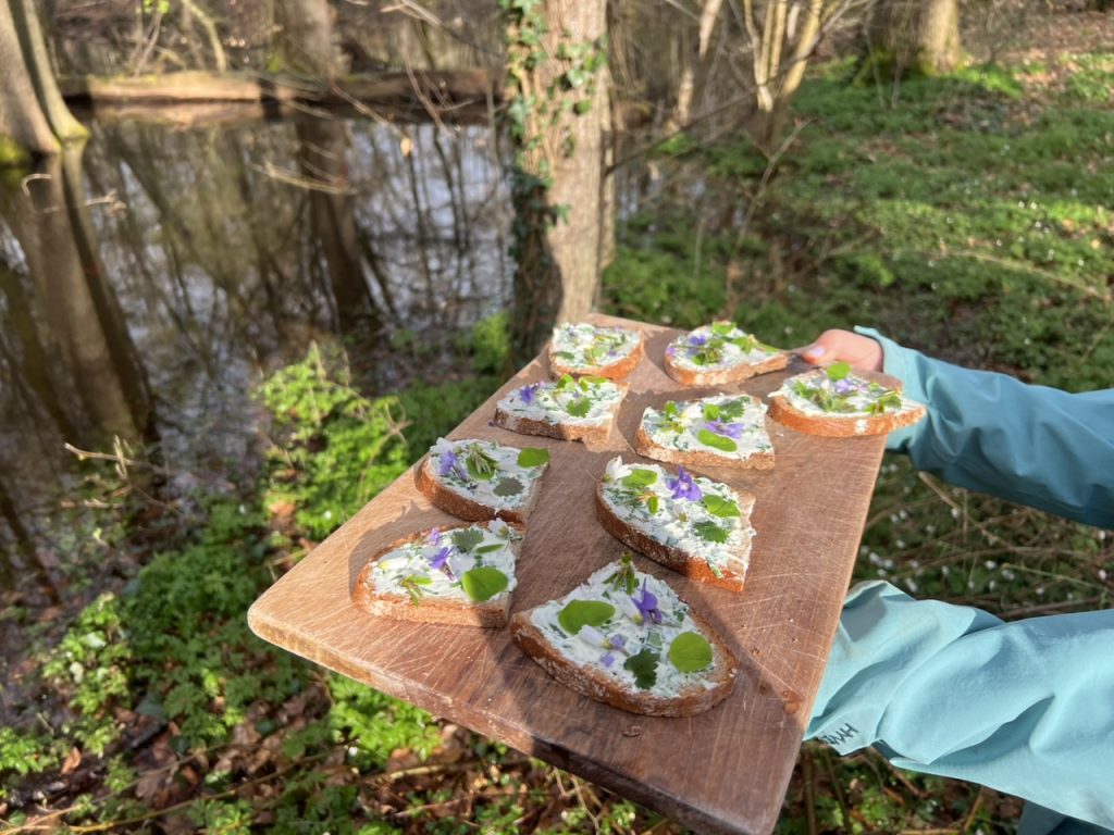 Ein Holzbrett mit Broten, belegt mit Wildkräutern und Blüten