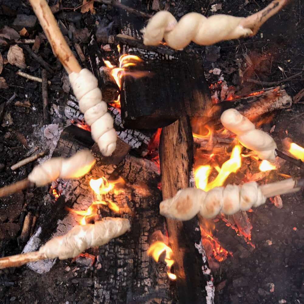 Stockbrot backt an Stöcken über der Glut eines Lagerfeuers