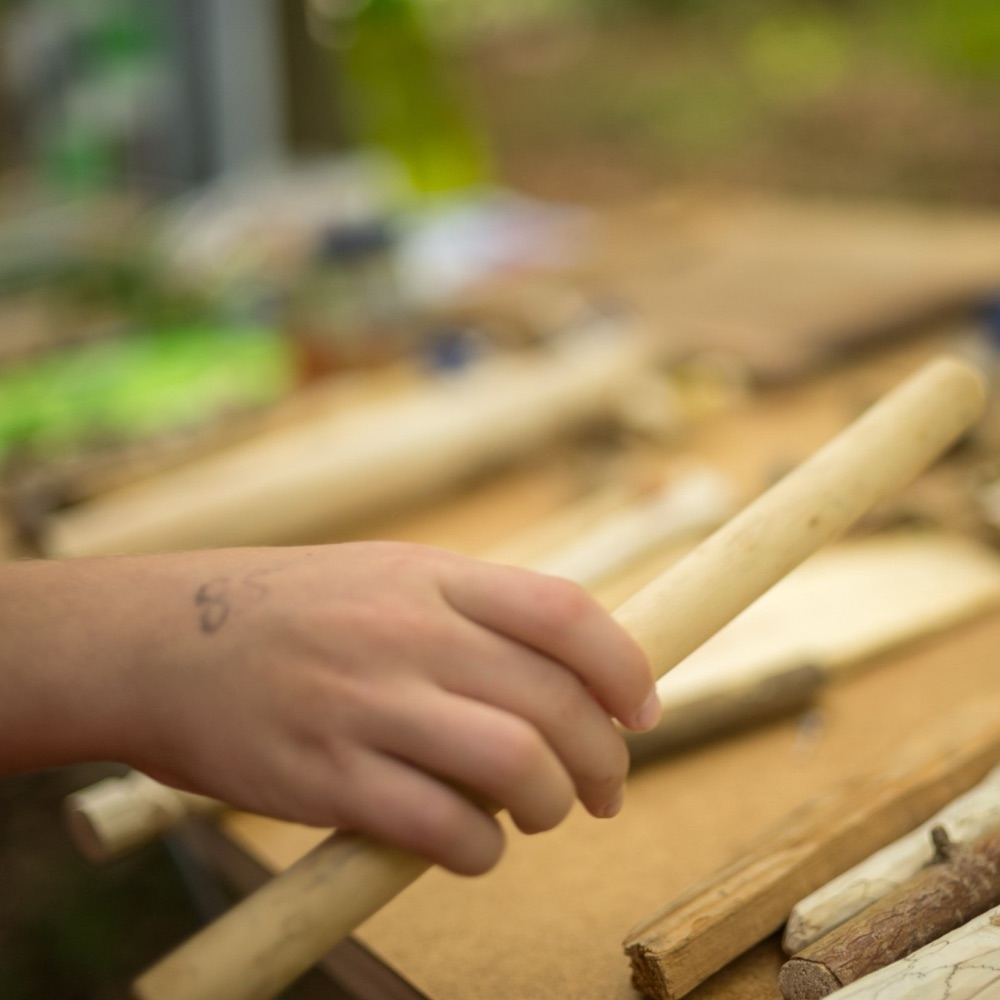 Eine Kinderhand greift nach einem geschnitzten Stock auf dem Werktisch im Wald